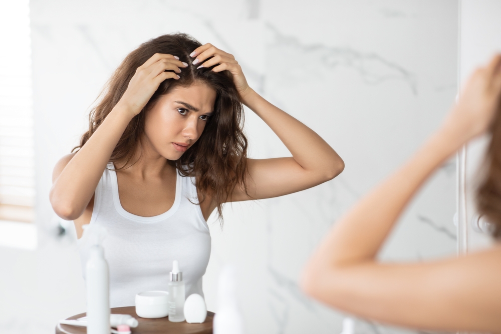 Woman examining her scalp in a mirror, concerned about hair loss.