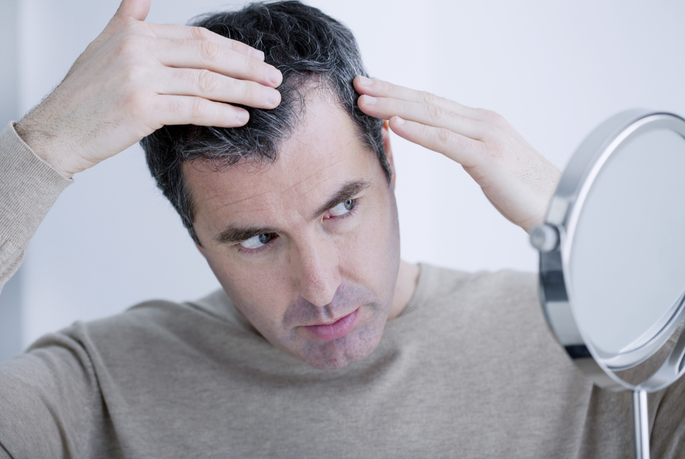 Man examines early hair loss in the mirror at his home.